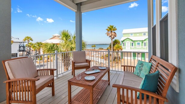 Eine Holzterrasse mit Tisch und Stühlen mit Blick auf einen Strand und grüne Gebäude.