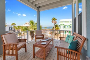 A wooden deck with a table and chairs, overlooking a beach and green buildings. - 🌴🌞4BR with Mulitple Decks | Walk to Beach + Soundside Access | Breezin Home (Navarre)