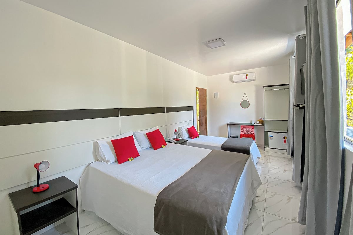 Ein Hotelzimmer mit zwei Betten, einem Schreibtisch, einem Spiegel und einem fenster mit Vorhängen.