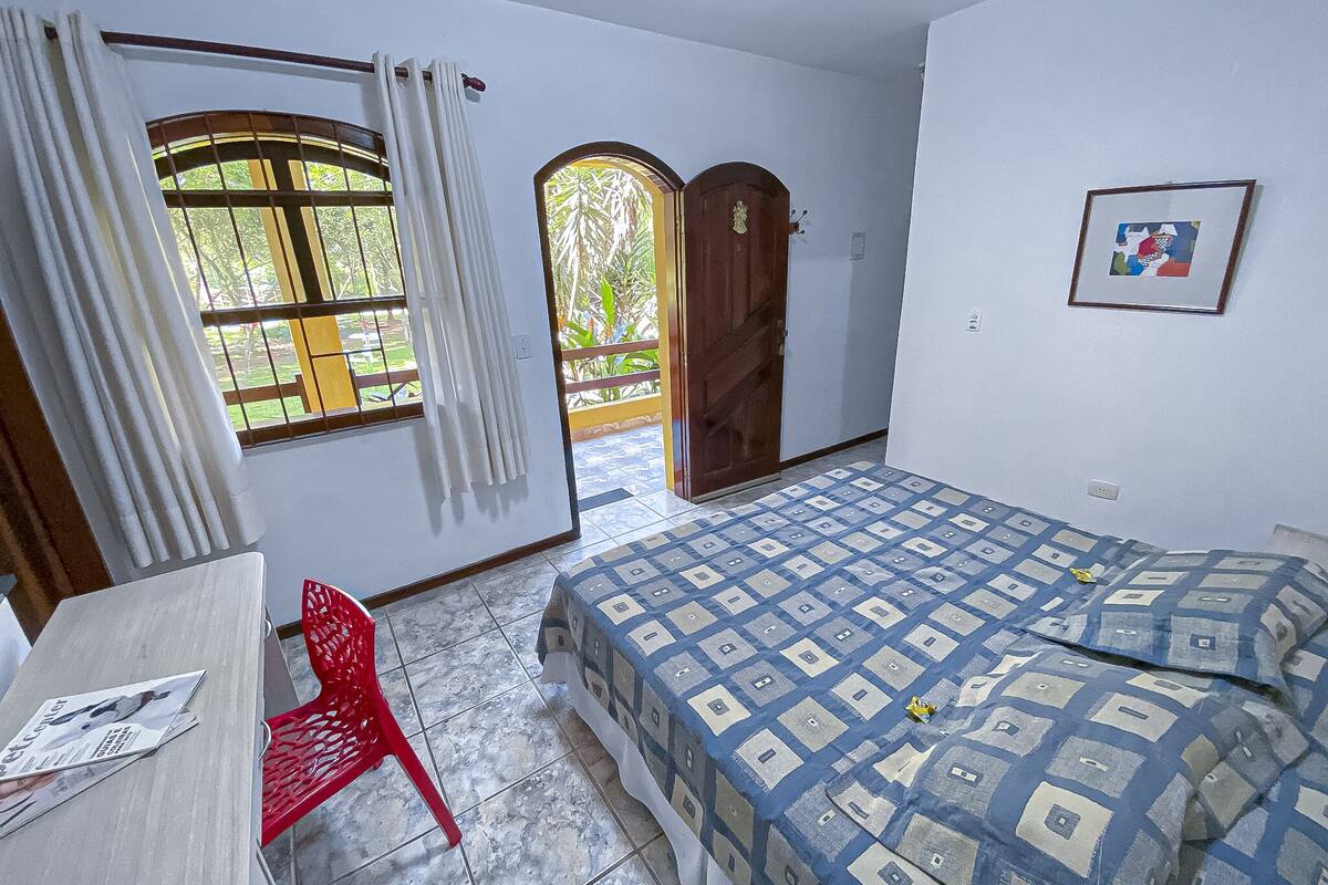 Ein Schlafzimmer mit Bett, Stuhl, Schreibtisch und einem Fenster mit Vorhängen.