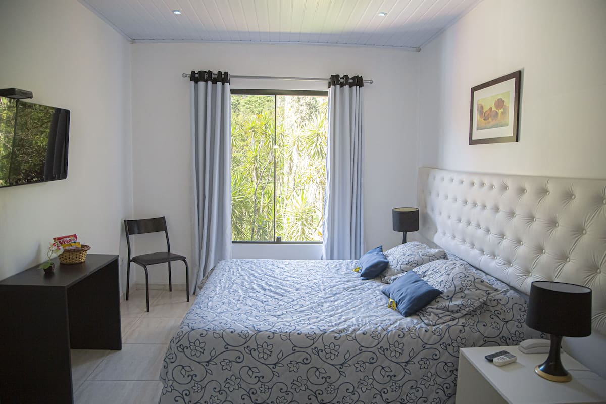 Ein Schlafzimmer mit einem großen Bett, einem Sessel, einem Schreibtisch und einem Fenster mit Vorhängen.
