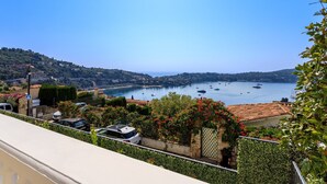 A coastal view with boats on the water, a car parked on a street, and greenery in the foreground. - VILLA  BELLE VUE VI4394 By Riviera Holiday Homes (Villefranche-sur-Mer)