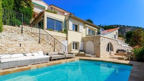 A poolside area with a stone wall, a staircase, and outdoor seating. - VILLA  BELLE VUE VI4394 By Riviera Holiday Homes (Villefranche-sur-Mer)