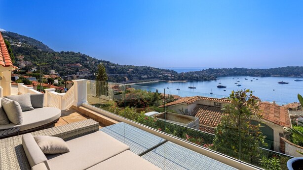 A balcony with outdoor seating, overlooking a bay with boats and a hilly landscape. - VILLA  BELLE VUE VI4394 By Riviera Holiday Homes (Villefranche-sur-Mer)