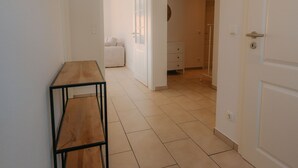 Ein Flur mit einer hölzernen Bank, einer Fußmatte und einer weißen Tür, die in ein Schlafzimmer führt.