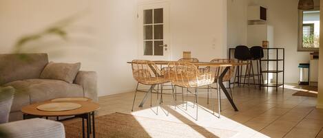 A modern living room with a sofa, a dining table with chairs, and a kitchen area in the background.