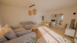 Ein modernes Wohnzimmer mit einer Eckcouch, einem Esstisch mit Stühlen und einer Küche im Hintergrund.