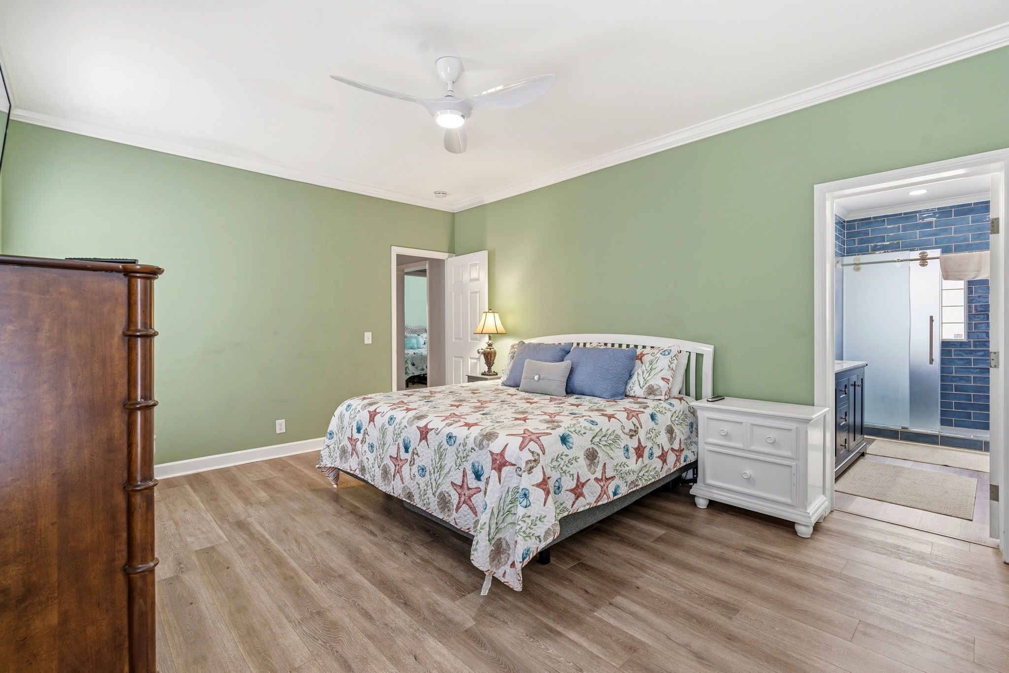 A bedroom with a bed, nightstands, a dresser, a ceiling fan, and a bathroom visible through an open door.