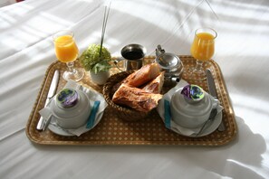 Uma bandeja de café da manhã com croissants, uma pequena planta, uma xícara de café, um copo de suco de laranja e um pote de iogurte.