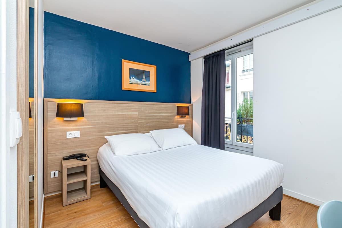 A modern hotel room with a large bed, wooden headboard, and two bedside lamps.