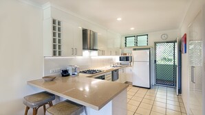 A modern kitchen with white cabinets, a central island with stools, a microwave, and a refrigerator. - Poinciana Lodge 207, Poinciana Lodge 207 on Hamilton Island (Hamilton Island)