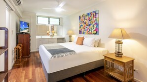 A hotel room with a large bed, a desk, a chair, a television, a lamp, and a colorful painting on the wall. - Poinciana Lodge 207, Poinciana Lodge 207 on Hamilton Island (Hamilton Island)