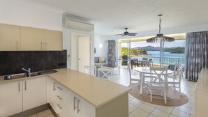 Una cocina moderna con una isla grande, un comedor con mesa y sillas, y un balcón con vistas al mar.