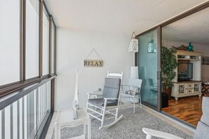 A balcony with a rocking chair, a small table, and a 'RELAX' sign. - Includes Xplorie Activities and Linens. PYRAMID - Upgraded 2BR oceanfront condo w/outdoor pool. (Ocean City)