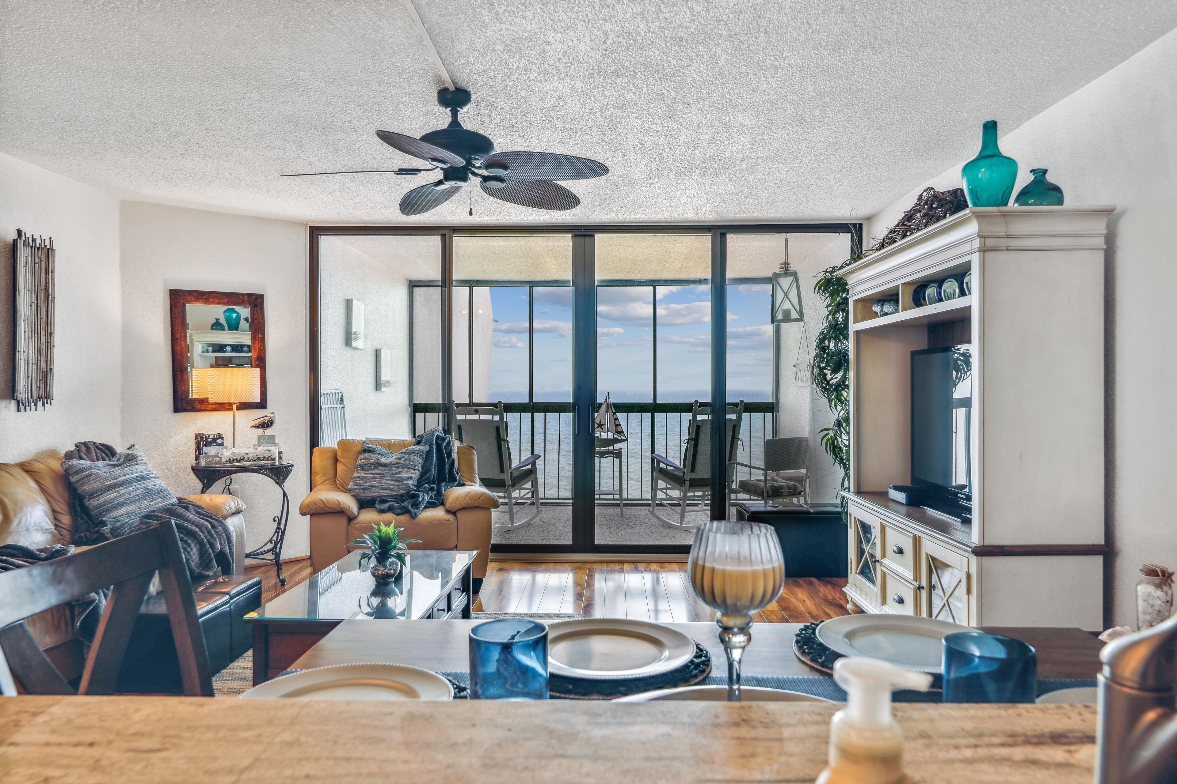 A modern living room with a dining area, large windows, and a view of the sea.