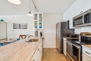 A modern kitchen with a marble countertop, stainless steel appliances, and a view of the ocean through a window. - Includes Xplorie Activities and Linens. PYRAMID - Upgraded 2BR oceanfront condo w/outdoor pool. (Ocean City)