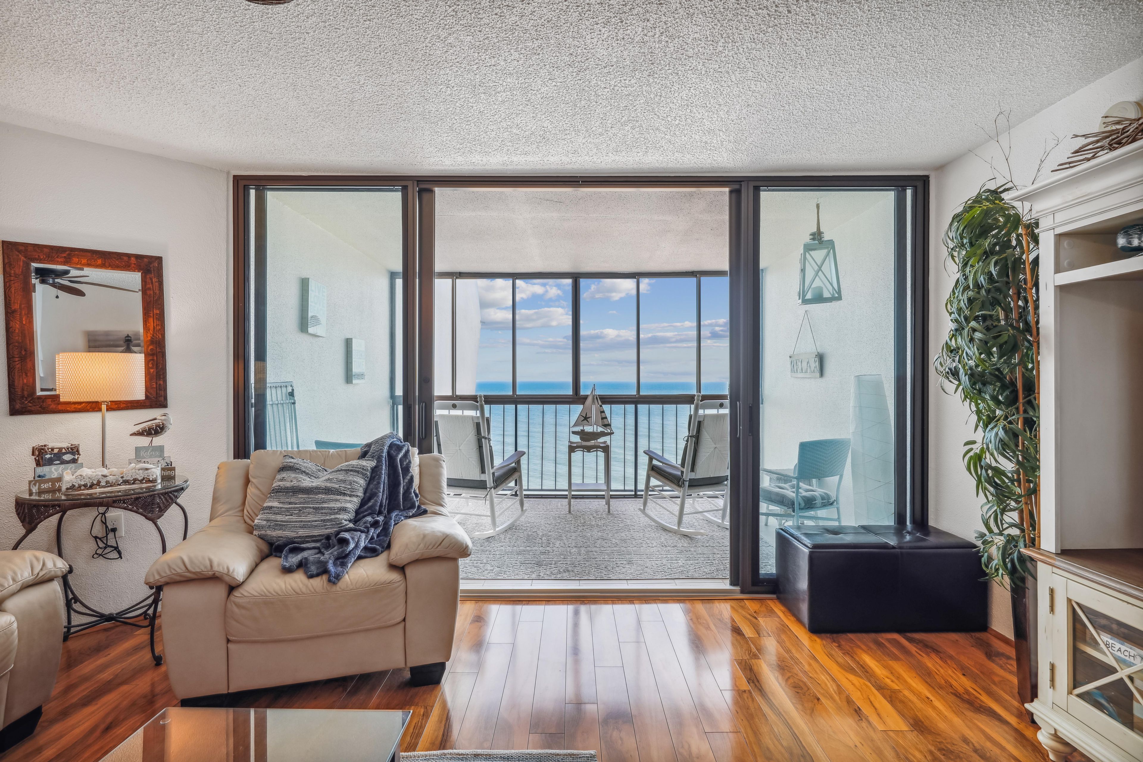 Un salon avec un canapé, une petite table et une vue sur la mer, visible à travers de grandes portes vitrées.