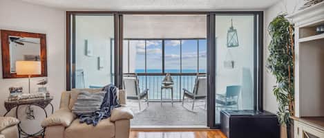 A living room with a sofa, a small table, and a view of the sea through large glass doors.