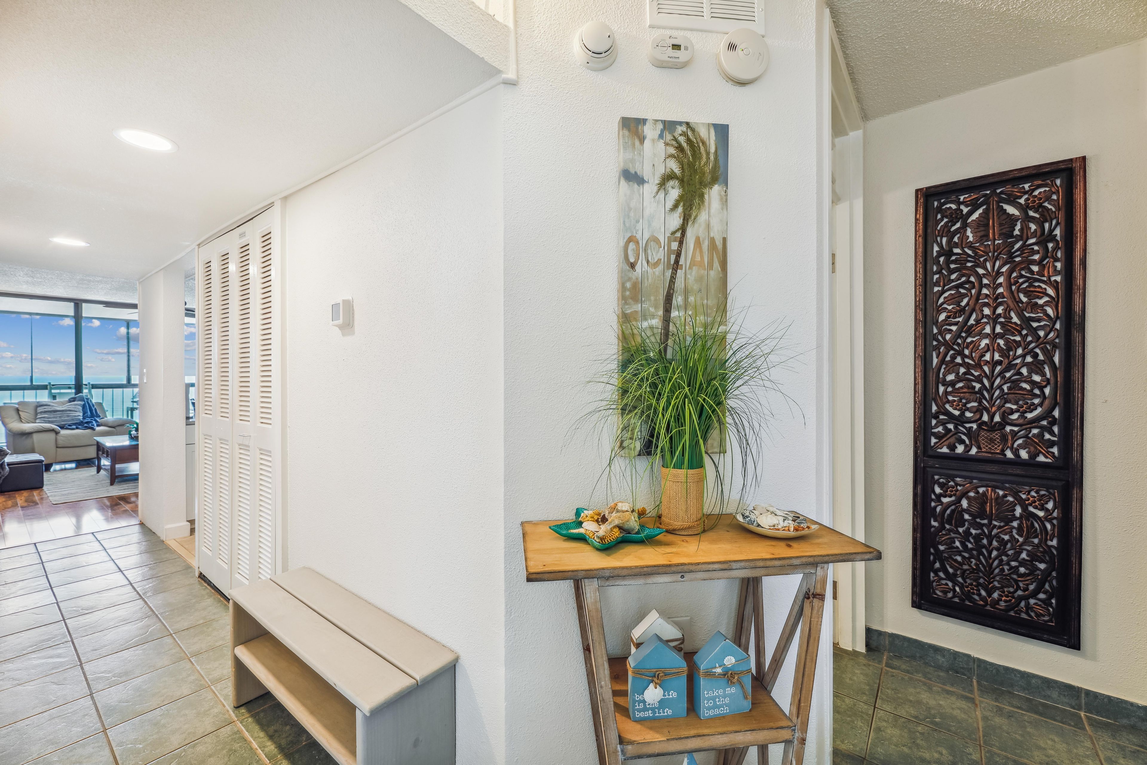 A hallway with a bench, a wall-mounted plant, decorative wall panels, and a view of the ocean through a window.