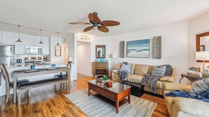 A modern kitchen with white cabinets, a dining table, and a ceiling fan. - Includes Xplorie Activities and Linens. PYRAMID - Upgraded 2BR oceanfront condo w/outdoor pool. (Ocean City)