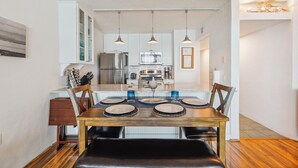 Een moderne keuken met roestvrijstalen apparatuur, een eethoek met een houten tafel en stoelen, en hangende lampen.