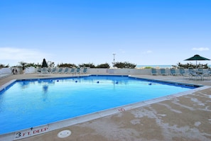 Une piscine rectangulaire dont la profondeur est indiquée à 3 pieds, entourée de chaises longues et de parasols, avec un ciel dégagé en arrière-plan.