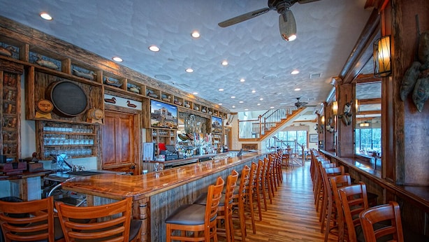 A bar area with wooden bar stools, a long counter, and a ceiling fan. - Decoys (Suffolk)