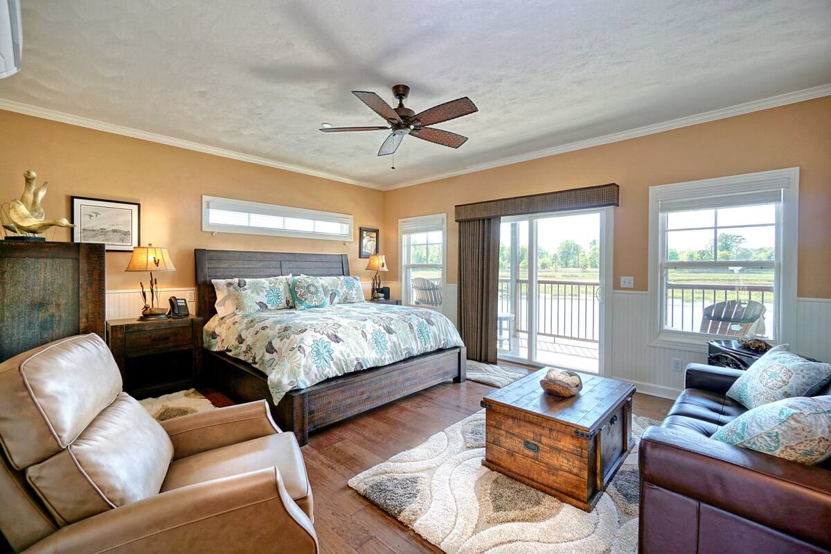 A bedroom with a large bed, a desk, a leather sofa, and a ceiling fan.