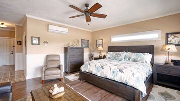 A bedroom with a large bed, a ceiling fan, a dresser, a chair, and a nightstand with a lamp.
