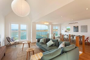 A spacious living room with a large green sofa, a wooden coffee table, and a view of the sea through large windows. - Appledore Home With Panoramic Estuary View (Bideford)