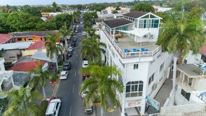 Un immeuble à plusieurs étages doté d’un balcon à l’étage supérieur, une rue bordée de voitures et de palmiers, et une vue sur les bâtiments environnants.