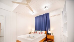 Une chambre à coucher avec un lit, des tables de chevet, un ventilateur de plafond et une fenêtre avec des rideaux.