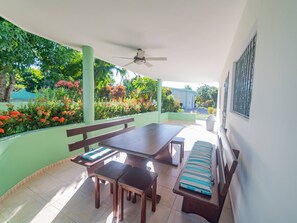A covered patio with a table, benches, and a ceiling fan.