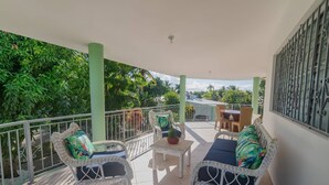 A covered balcony with wicker furniture, a small table, and a view of greenery. - 7br Massive Villa In Sosúa - 2mins From Nightlife! (Sosúa)