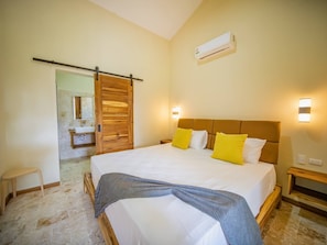 A bedroom with a bed, bedside tables, a mirror, and an air conditioning unit. - Sun & Soul - Caribbean 9br Villa In Sosúa! (Sosúa)