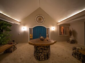 A spacious room with a high ceiling, a central stone table, and a blue door. - Sun & Soul - Caribbean 9br Villa In Sosúa! (Sosúa)