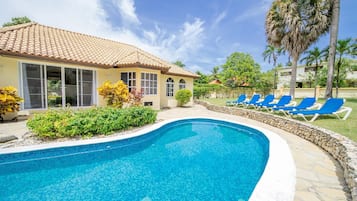 Une piscine aux carreaux bleus, une maison avec un toit en tuiles et des fauteuils de jardin bleus.