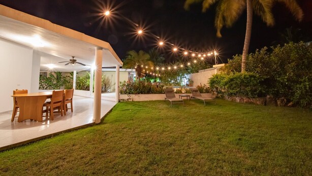 Een modern terras buiten met een eethoek, sfeerverlichting en weelderige begroeiing.