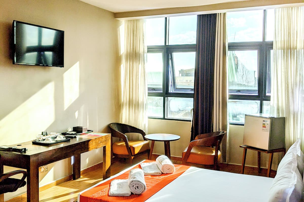 A hotel room with a bed, a desk, a chair, a TV, and a window with curtains.