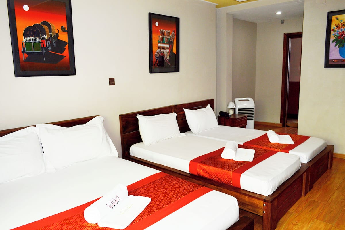 A hotel room with two beds, each with white linens and red accents, a wooden headboard, and artwork on the walls.