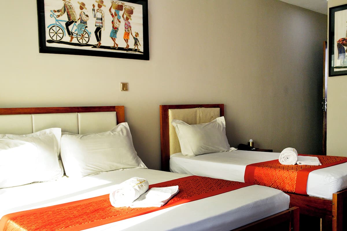 A hotel room with two single beds, each with white linens and red bedspreads. There is a framed picture on the wall above the beds.