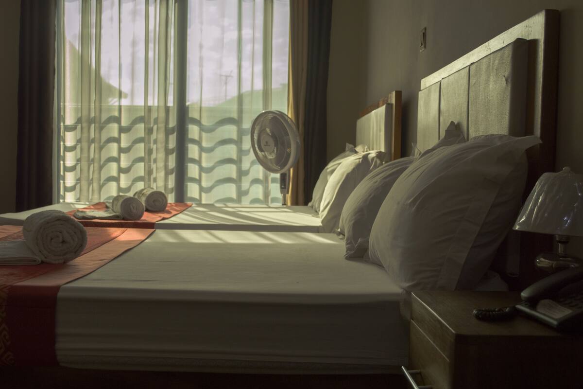 A hotel room with a bed, a bedside table with a lamp, and a window with curtains.