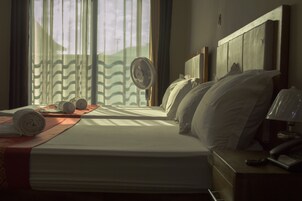 Una habitación de hotel con una cama, una mesita de noche con lámpara y una ventana con cortinas.