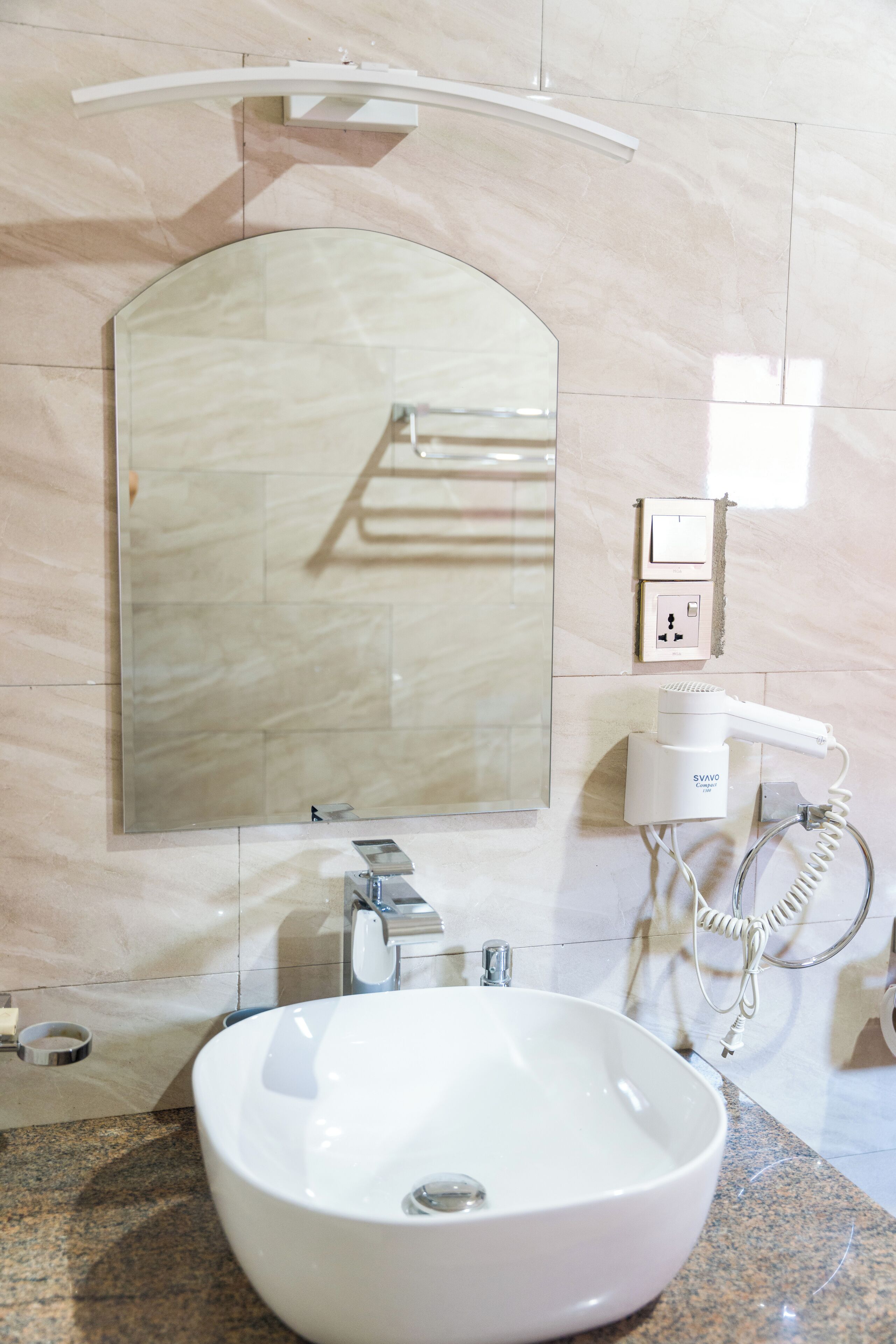 A bathroom with a large mirror, a sink, and a hairdryer on a wall-mounted charging station.