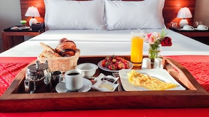 Una bandeja de desayuno bien dispuesta con pan, fresas, café y jugo, sobre una cama con sábanas blancas y cabecera de madera.