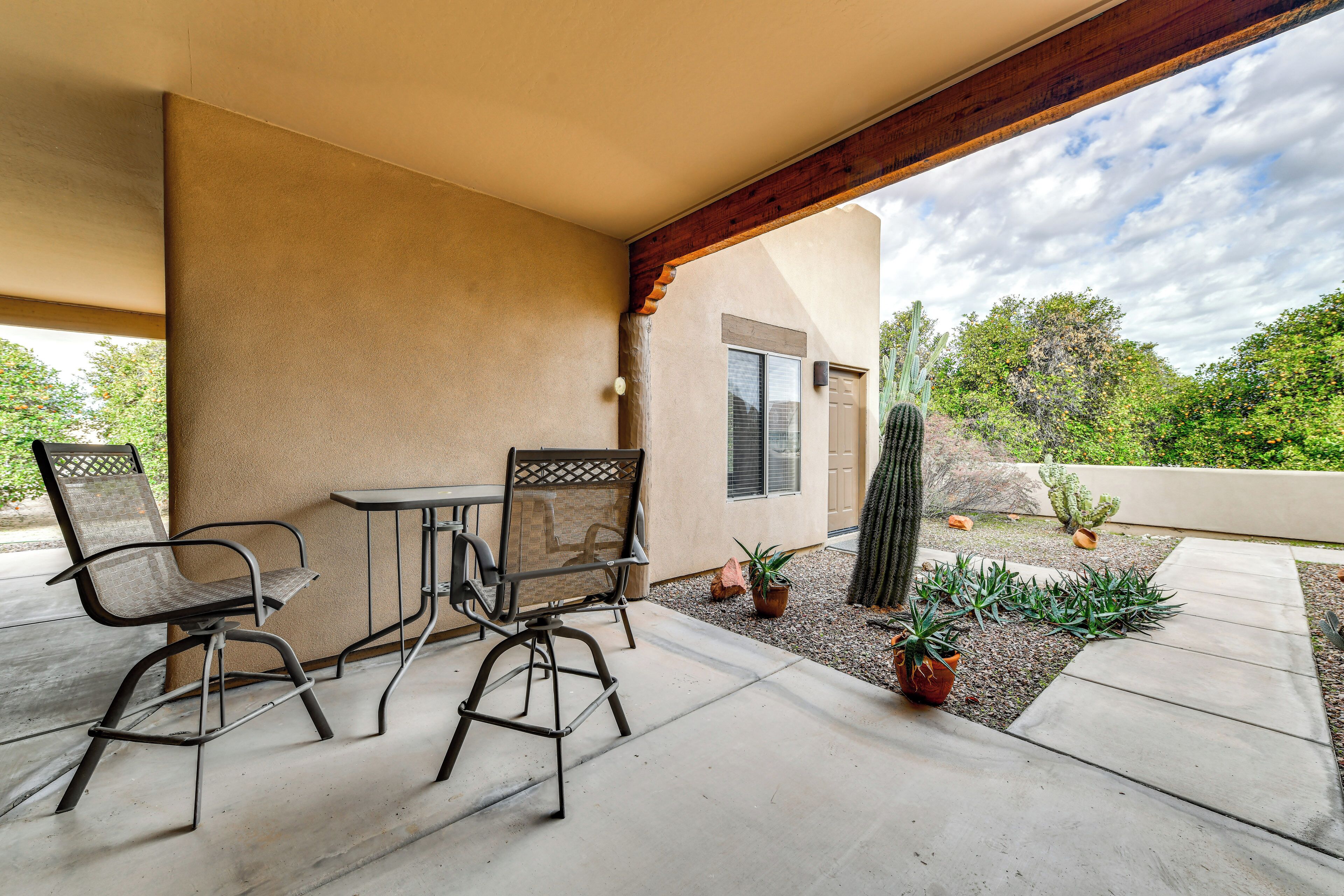 A covered patio with two metal chairs and a table, surrounded by potted plants and a cactus garden.