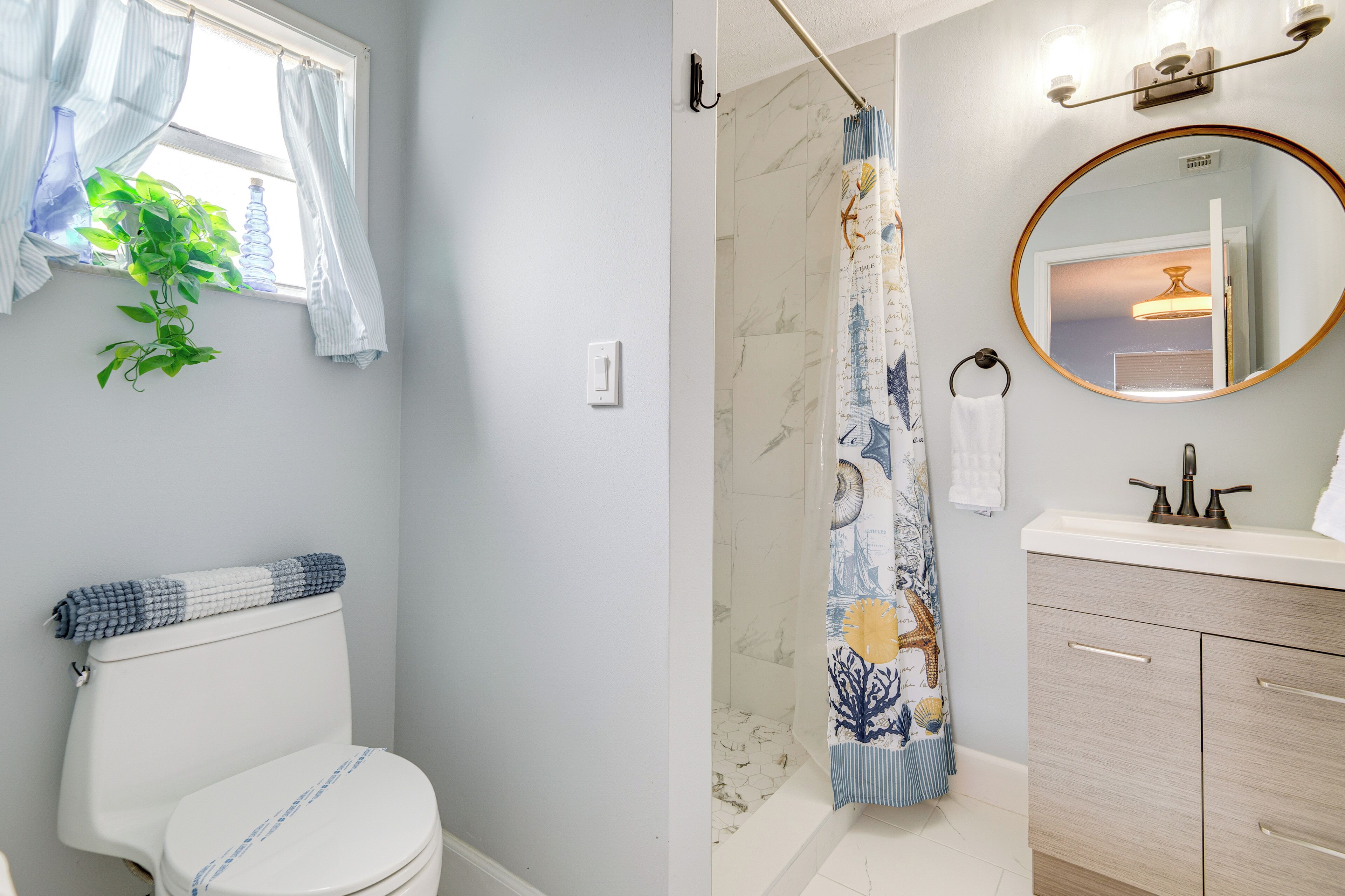 A bathroom with a toilet, shower curtain, sink, and mirror.