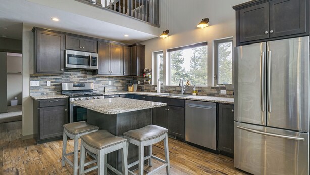 A modern kitchen with dark cabinetry, stainless steel appliances, and a large island with stools. - Hike + Ski: Grand Lake Cabin w/ Mtn-view Deck (Grand Lake)