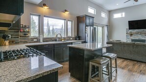 A modern kitchen with granite countertops, dark cabinetry, and a large island with bar stools. - Hike + Ski: Grand Lake Cabin w/ Mtn-view Deck (Grand Lake)