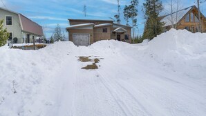A snow-covered driveway leading to a two-story wooden house with a garage. - Hike + Ski: Grand Lake Cabin w/ Mtn-view Deck (Grand Lake)